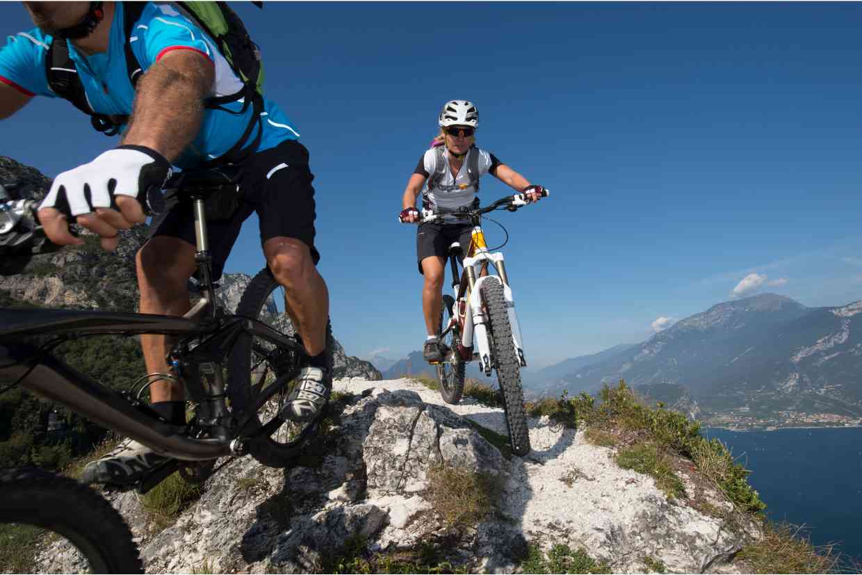Dois ciclistas em trilha de montanha, ambos usando capacetes MIPS em cenário de alto relevo.