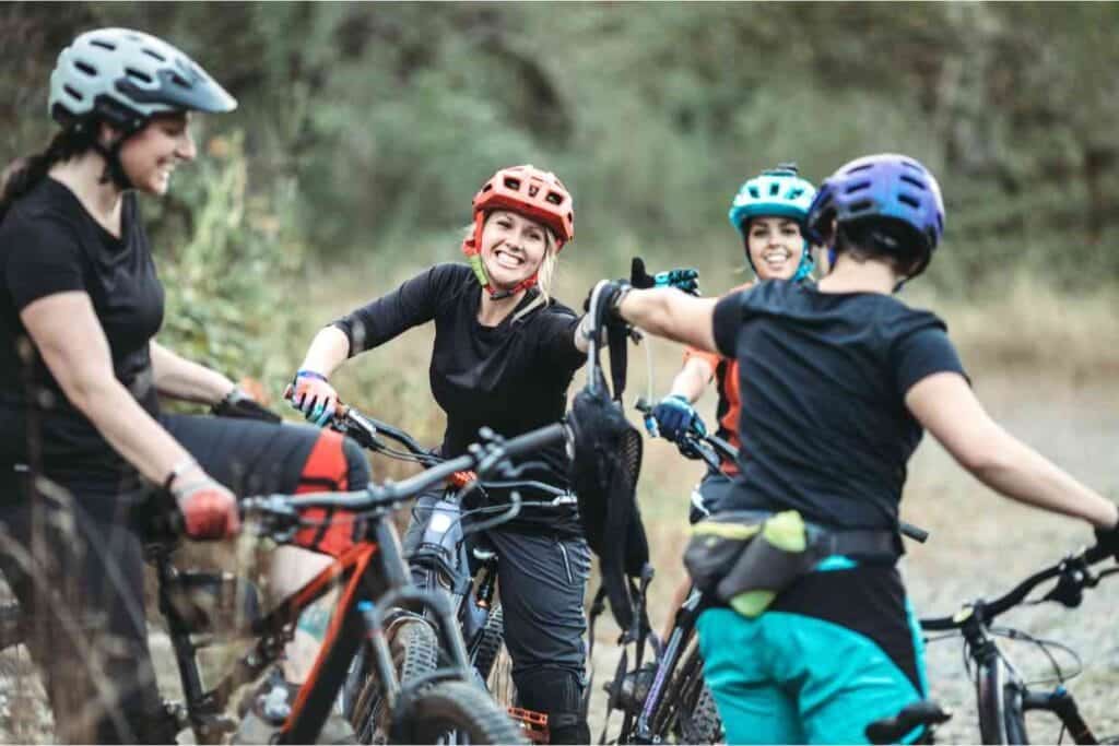 Grupo de ciclistas mulheres com capacete MTB fazendo uma pausa durante trilha em meio à natureza.
