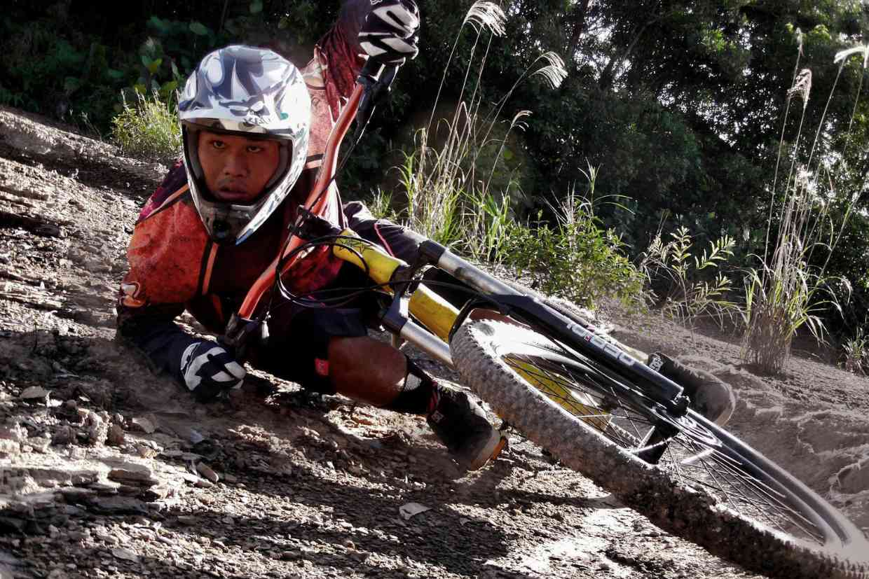 Ciclista usando capacete downhill branco em queda durante descida agressiva na trilha.