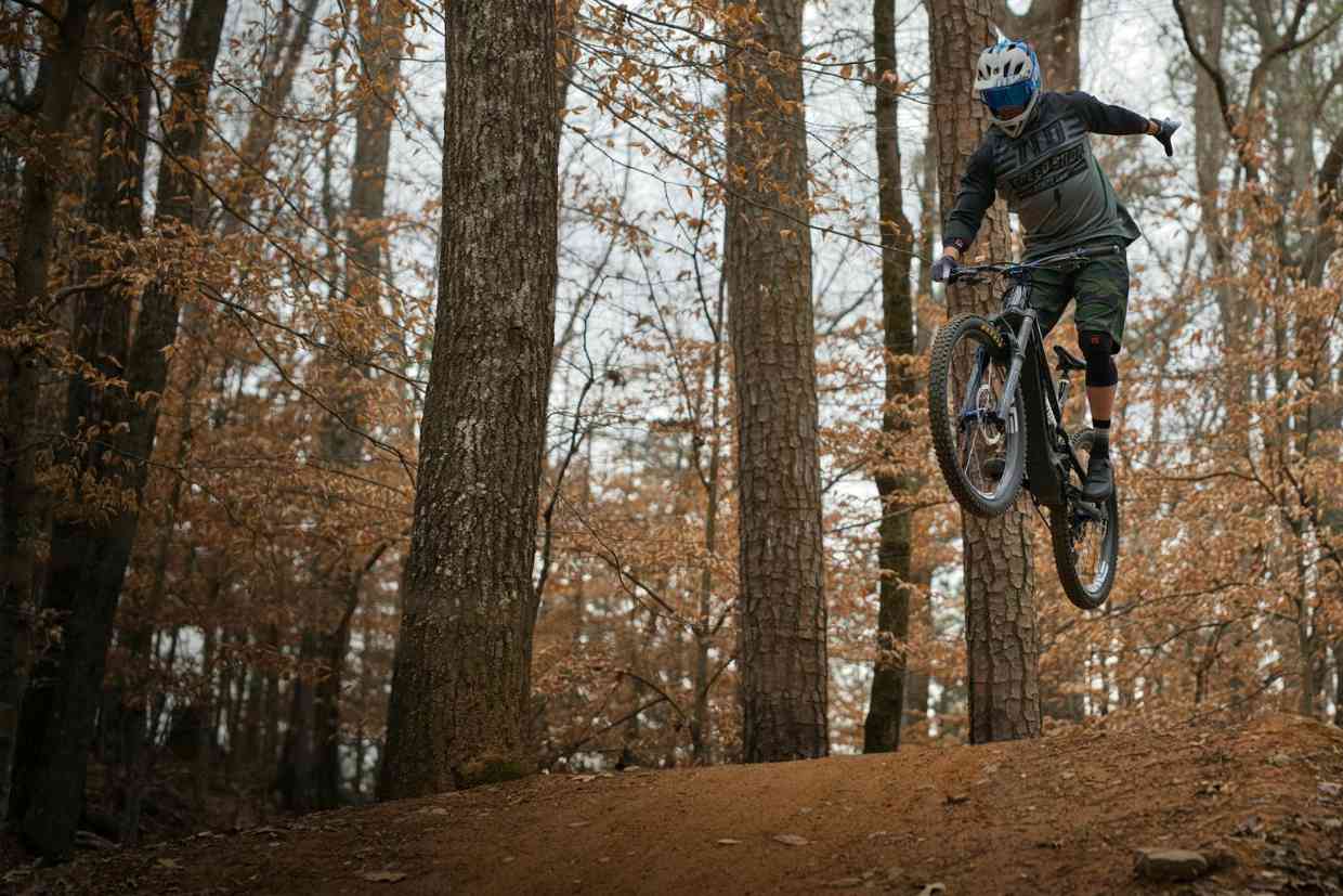 Ciclista em salto elevado em floresta usando capacete downhill azul com viseira.