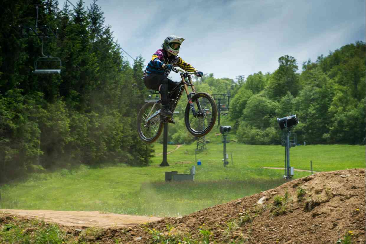 Ciclista saltando em pista de MTB com capacete downhill e roupas coloridas.