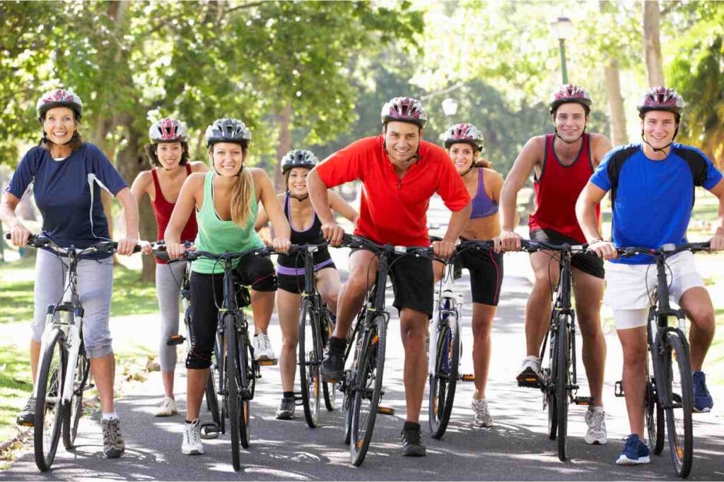 Grupo de ciclistas sorrindo em parque durante treino para emagrecer pedalando Legenda: Pedalar em grupo é uma forma divertida e eficaz de emagrecer pedalando e manter a motivação em alta.