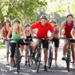 Grupo de ciclistas sorrindo em parque durante treino para emagrecer pedalando Legenda: Pedalar em grupo é uma forma divertida e eficaz de emagrecer pedalando e manter a motivação em alta.