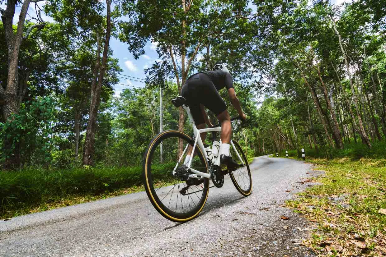 Ciclista subindo ladeira íngreme cercada por vegetação, exigindo esforço intenso e gerando fadiga muscular.