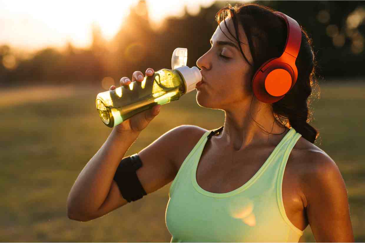 Ciclista se hidrata durante treino ao entardecer, prevenindo a fadiga muscular com ingestão de líquidos.