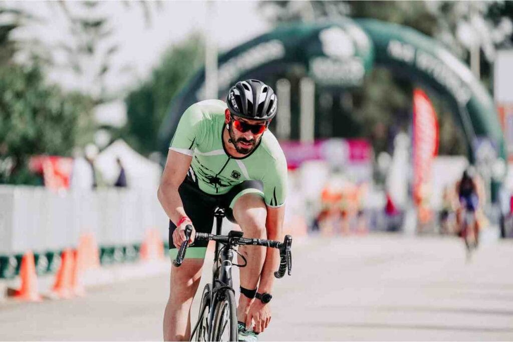 Ciclista se apoia exausto na bike após prova intensa, sinal de fadiga muscular no final da corrida.