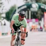 Ciclista se apoia exausto na bike após prova intensa, sinal de fadiga muscular no final da corrida.
