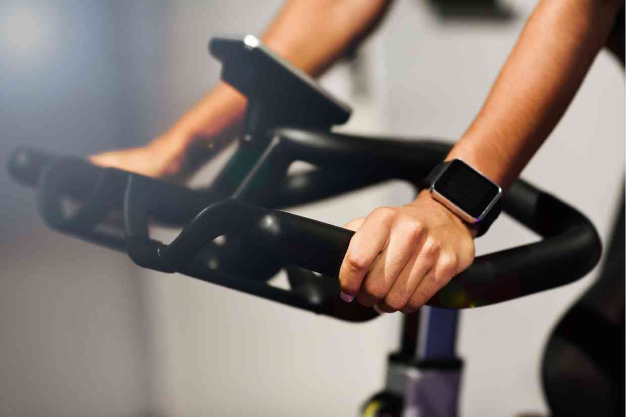 Mãos segurando uma bicicleta indoor com smartwatch, ideal para sincronização com Garmin Edge 540.