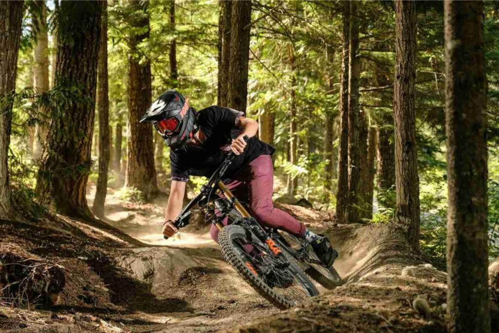 Ciclista usando capacete integral realizando curva fechada em trilha de mountain bike com solo batido.