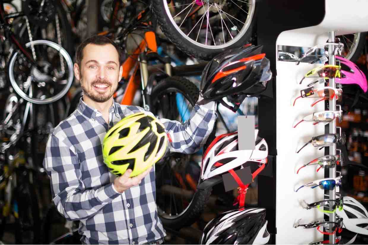 Vendedor segurando modelos de capacete inteligente em loja de bicicletas.