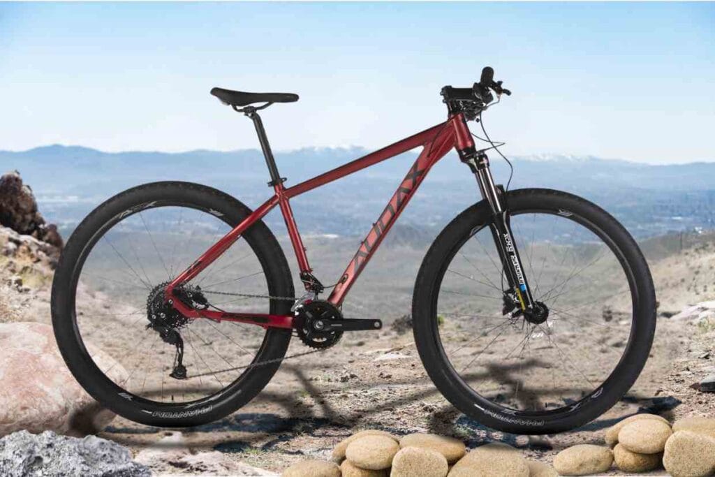 Bicicleta Audax ADX 100 vermelha em um terreno montanhoso com pedras e vista panorâmica.