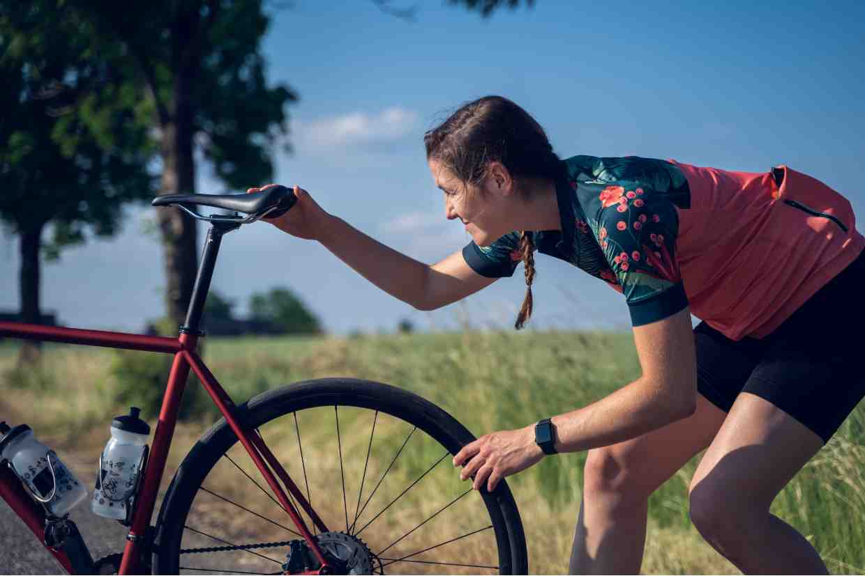 Mulher ajustando a posição do selim de bicicleta em área rural ao ar livre.