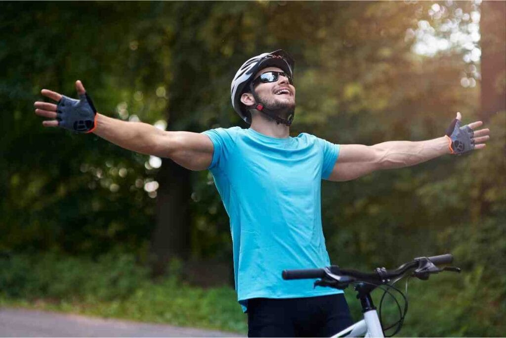 Ciclista comemorando com braços abertos após pedalada ao ar livre, com conforto do bike fit feito.