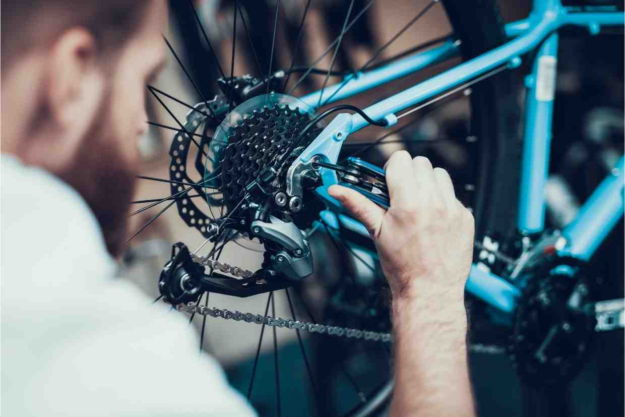 Mecânico ajustando o câmbio traseiro de uma bicicleta azul com precisão. O ajuste fino da transmissão também faz parte do bike fit, garantindo eficiência ao pedalar.