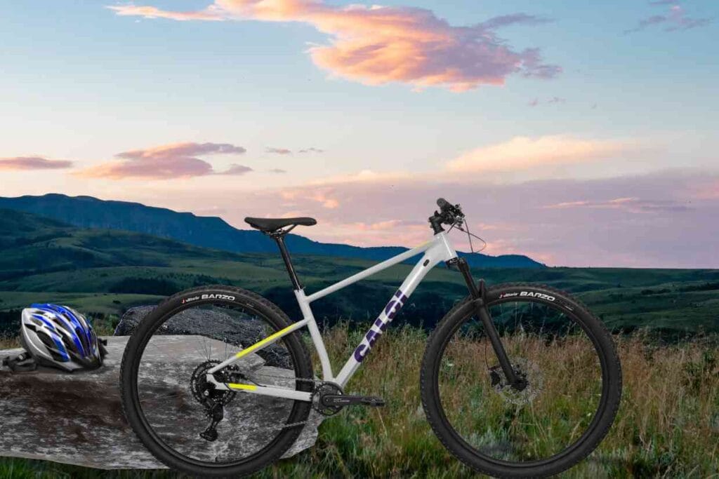 Bicicleta Caloi Explorer Comp branca posicionada sobre uma pedra com capacete ao lado e paisagem de montanhas ao fundo.