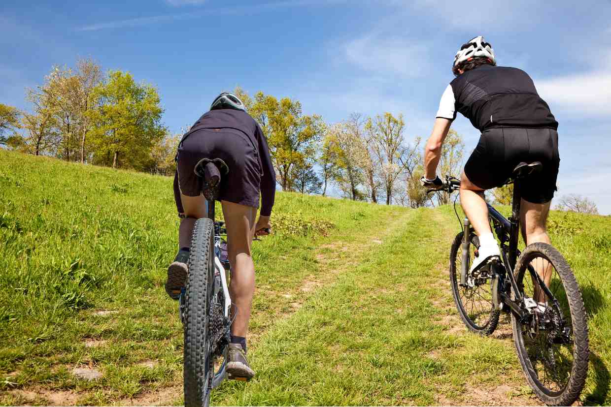 Dois ciclistas pedalando lentamente por uma trilha de MTB inclinada com suas bicicletas de mountain bike para iniciantes.