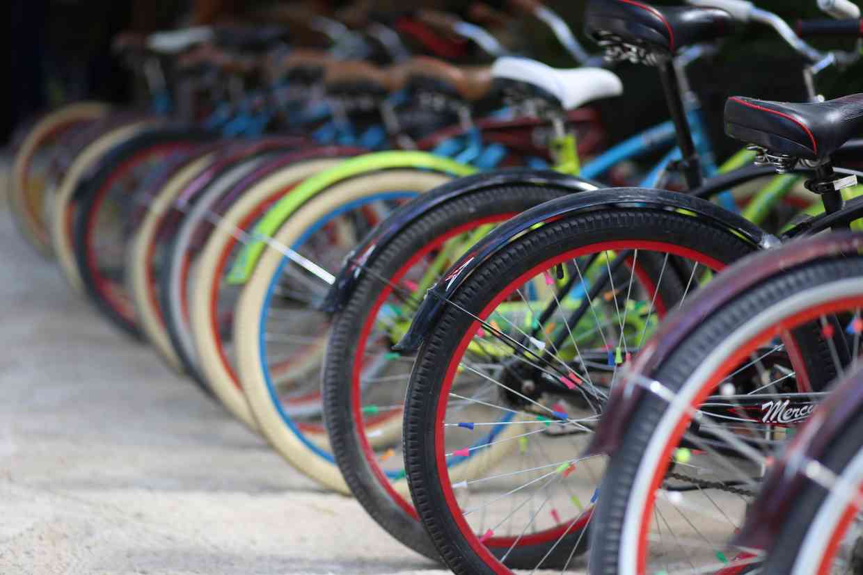 Linha de bicicletas coloridas estacionadas lado a lado com foco nas rodas que atendem a diferentes ciclistas com a variedade do tamanho de bicicleta escolhida.