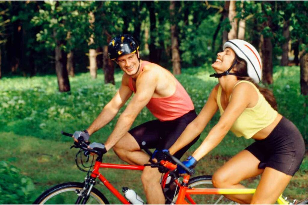 Casal pedalando juntos em área verde, sorrindo e aproveitando o passeio com suas bicicletas de tamanhos ajustados para maior segurança e conforto.