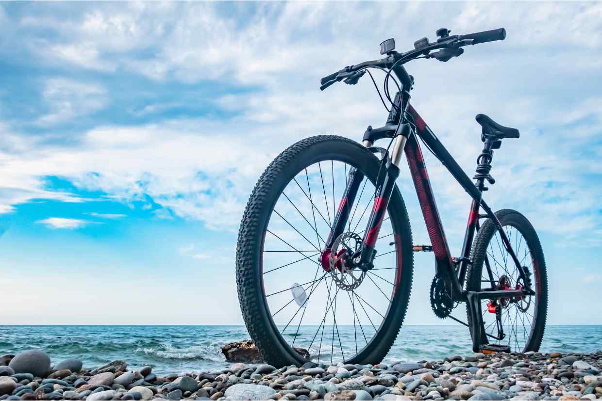 Bicicleta aro 29 estacionada sobre pedras à beira-mar ao lado do oceano, mostrando o upgrade bike feito.