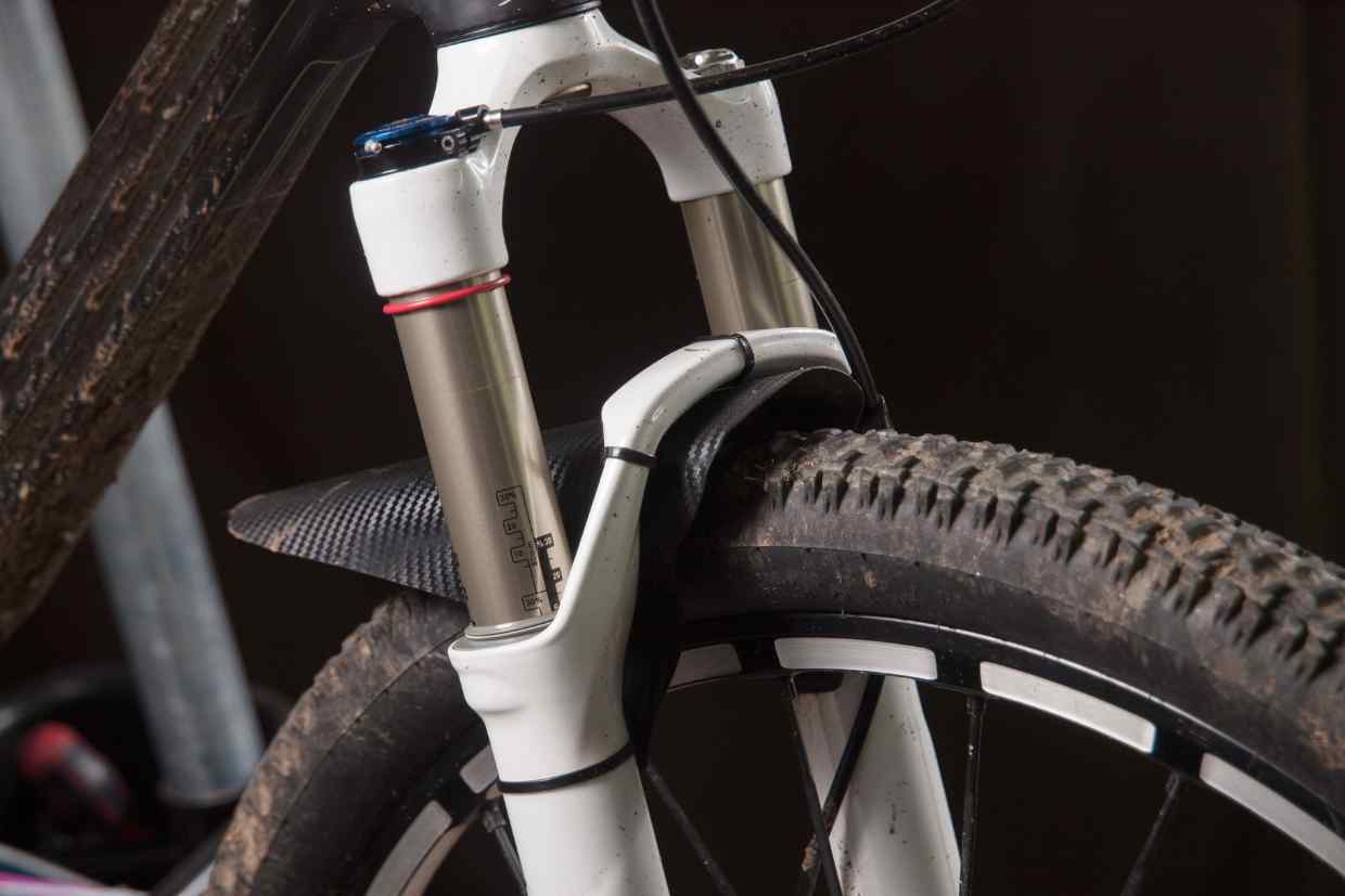 Detalhe do garfo de suspensão dianteira de uma mountain bike com lama nos pneus, num upgrade feito na bike.