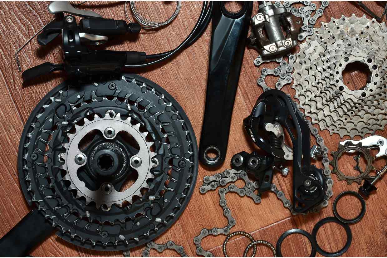 Componentes de bicicleta desmontados: pedivela, câmbios, correntes e catracas espalhados em fundo de madeira, itens necessários a um upgrade bike.