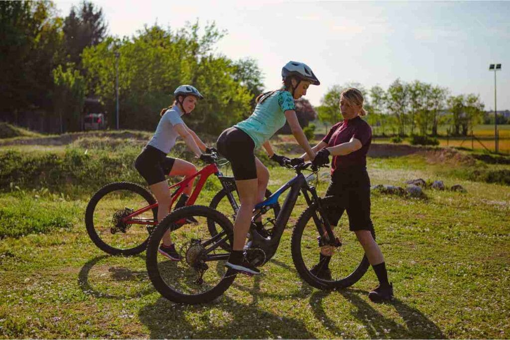Imagens de duas alunas numa aula com suas bicicletas mountain bike aprendendo movimentos básicos com seu instrutor.