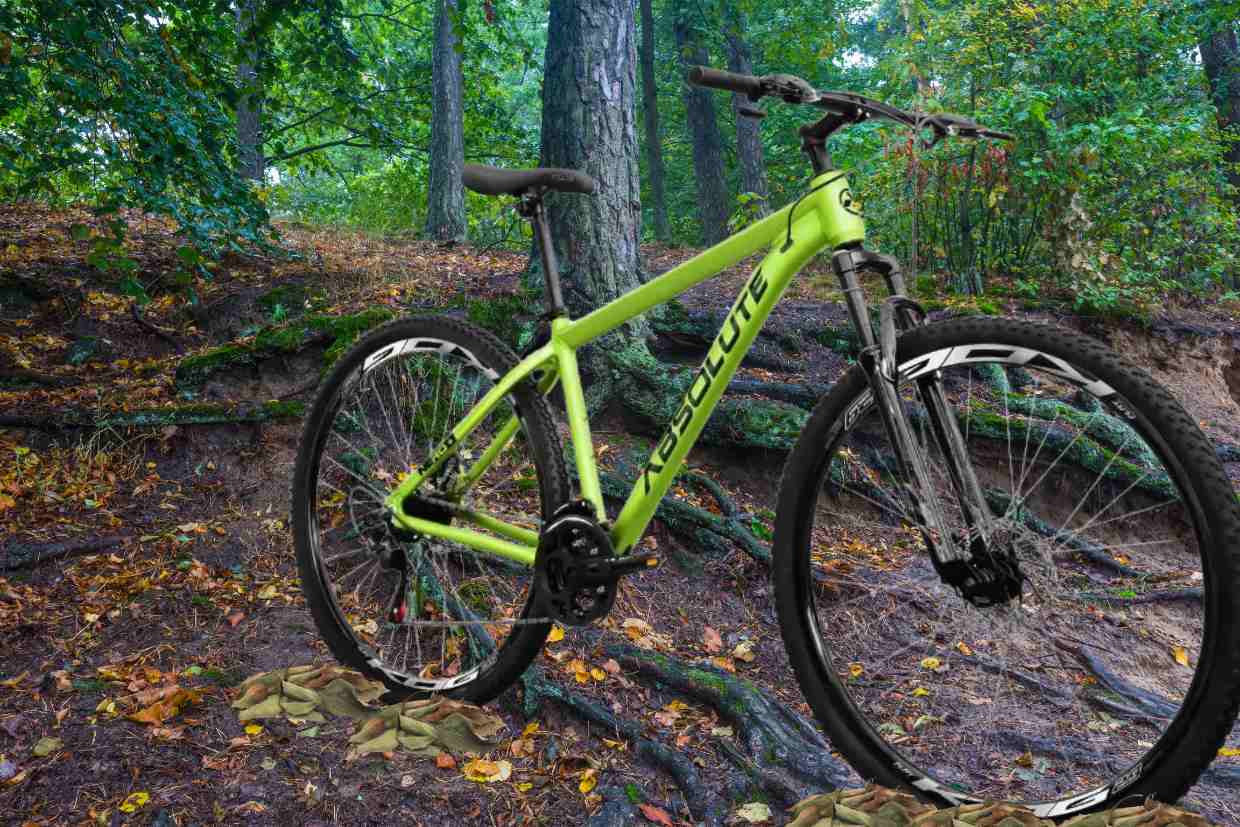 Bicicleta aro 29 Absolute Nero amarela posicionada em trilha acidentada com raízes expostas.