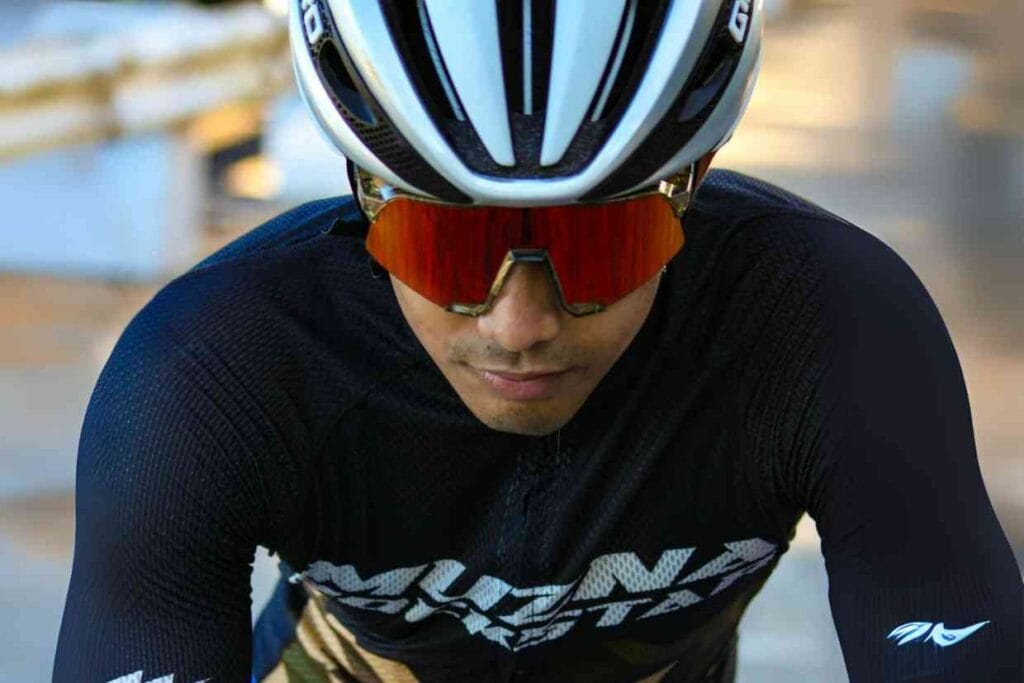 Imagem frontal de ciclista usando um capacete de ciclismo Giro Cinder MIPS branco e óculos de ciclismo, enquanto pedala.