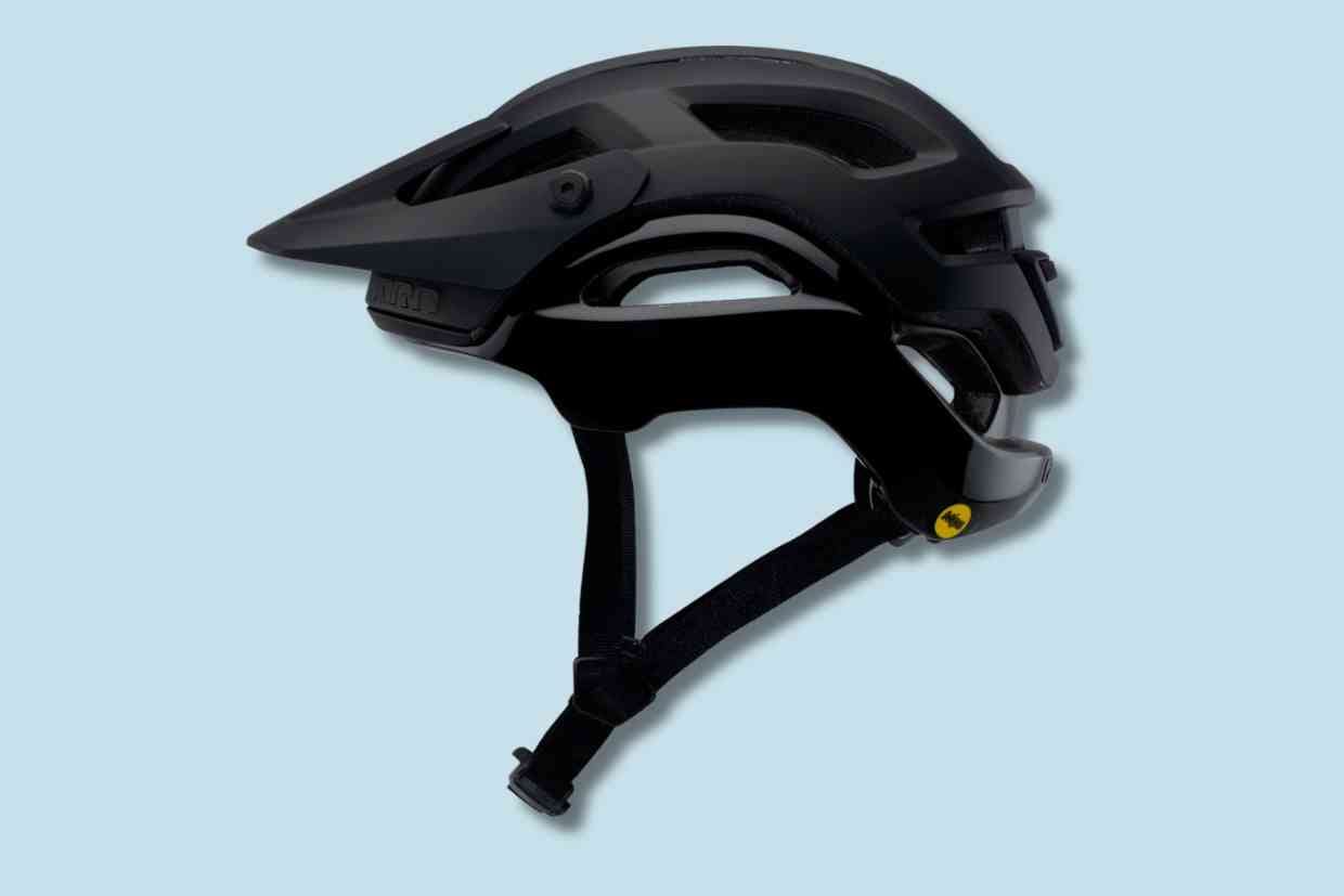 Capacete Giro Manifest Spherical preto numa vista lateral e sobreado num fundo azul claro.