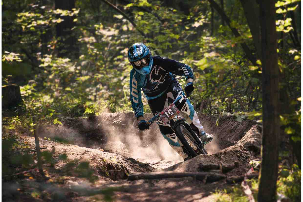Ciclista com roupa de competição usando capacete para MTB em trilha de terra em alta velocidade.