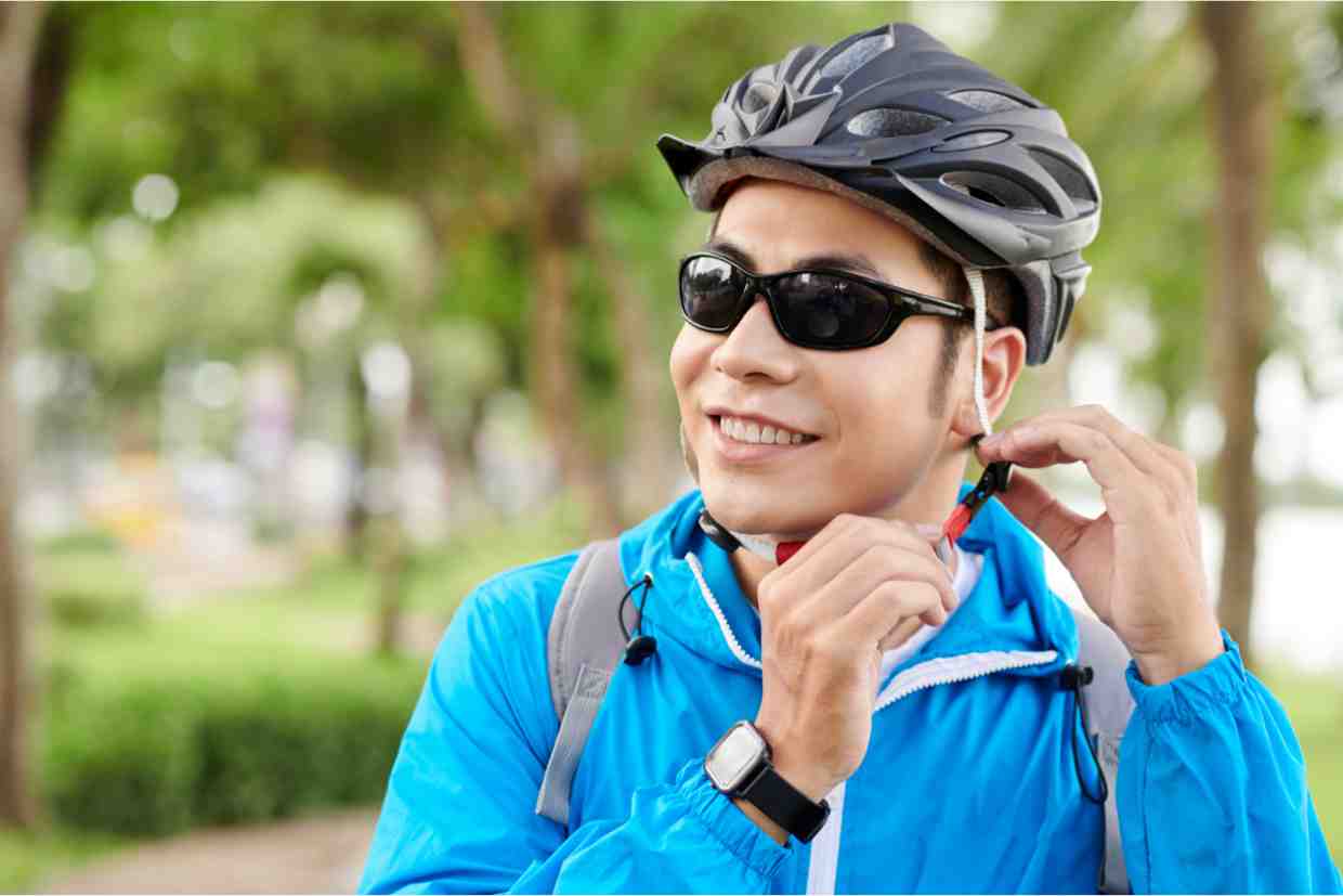 Ciclista sorridente ajustando capacete para MTB em parque arborizado.