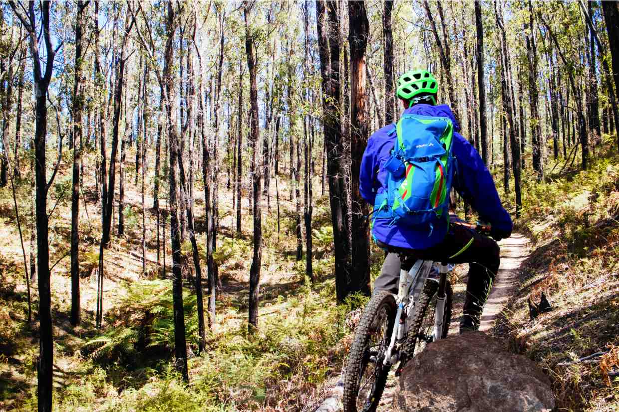 Ciclista com mochila e capacete pedalando com a Groove Hype 70 em floresta densa.