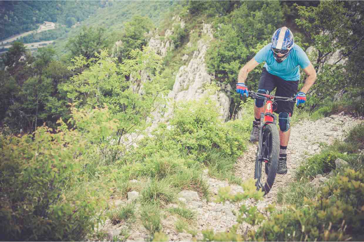 Ciclista subindo trilha técnica com a bike Groove Hype 70 em terreno rochoso e íngreme.