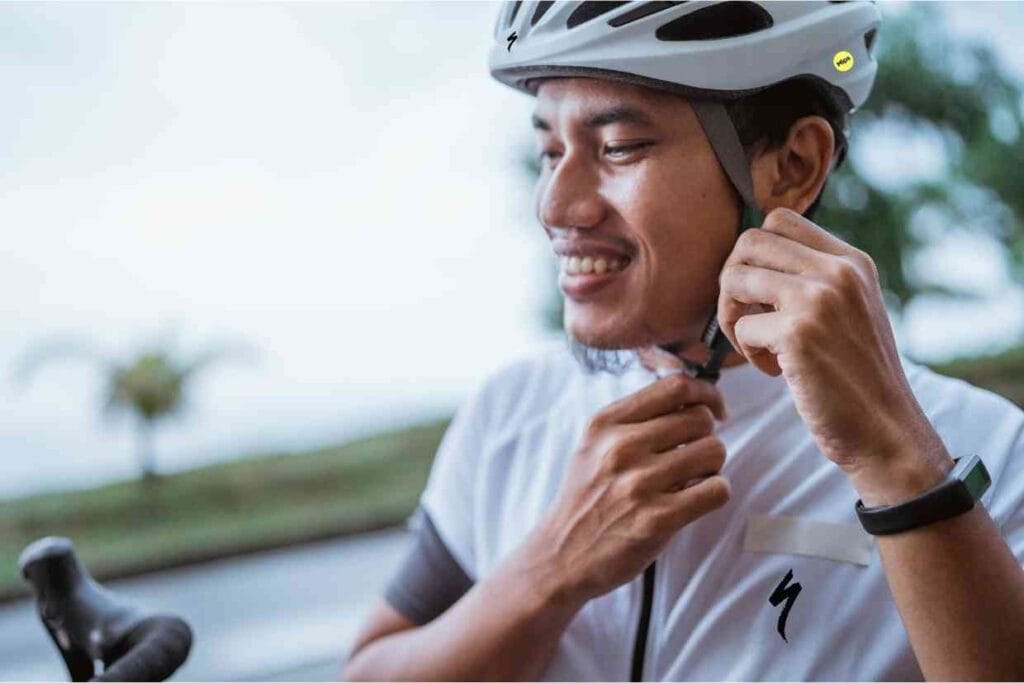 Ciclista usando uma camisa branca ajusta seu capacete Specialized Align II na cabeça ao lado da sua bicicleta.