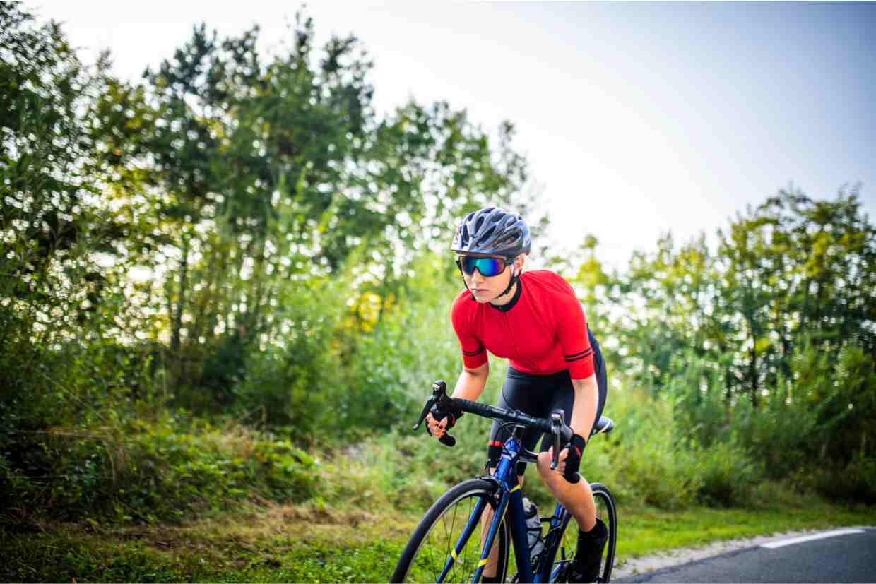 Ciclista vestido com jersey vermelho pedalando numa estrada inclinada cercada por árvores, exemplo de pedalar em subidas longas.