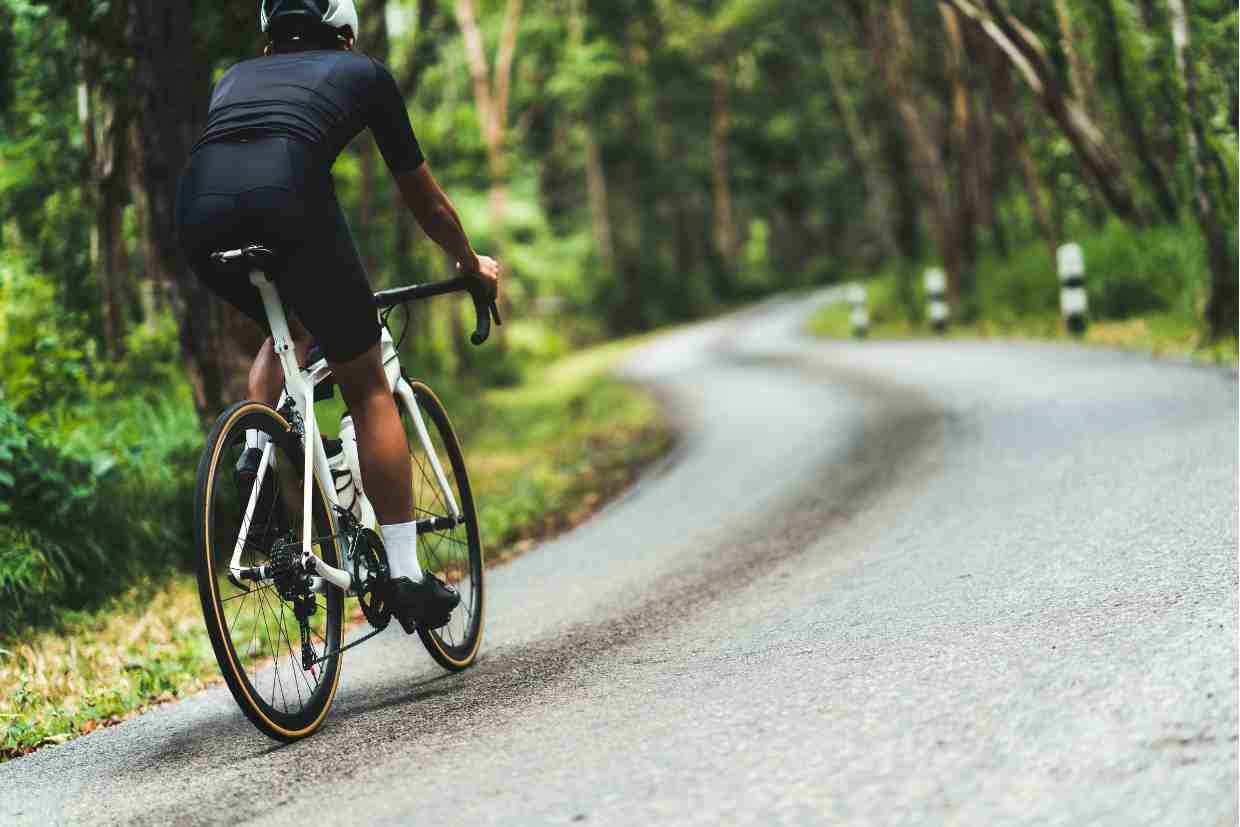 Vista traseira de ciclista com bike de estrada subindo curva em asfalto, representando a performance de pedalar em subidas.