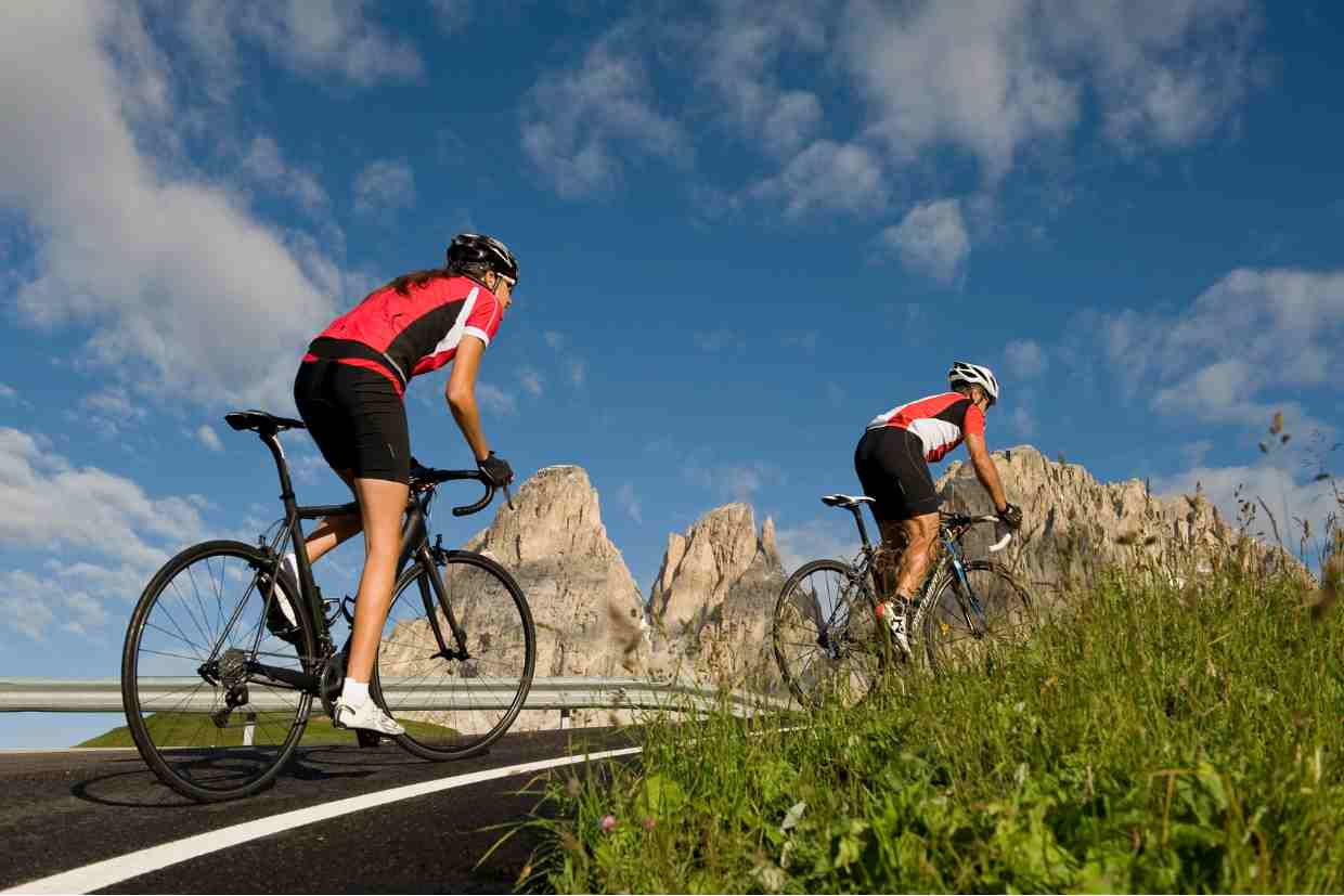 Dupla de ciclistas subindo encosta íngreme com bikes de estrada, simbolizando esforço coletivo ao pedalar em subidas.