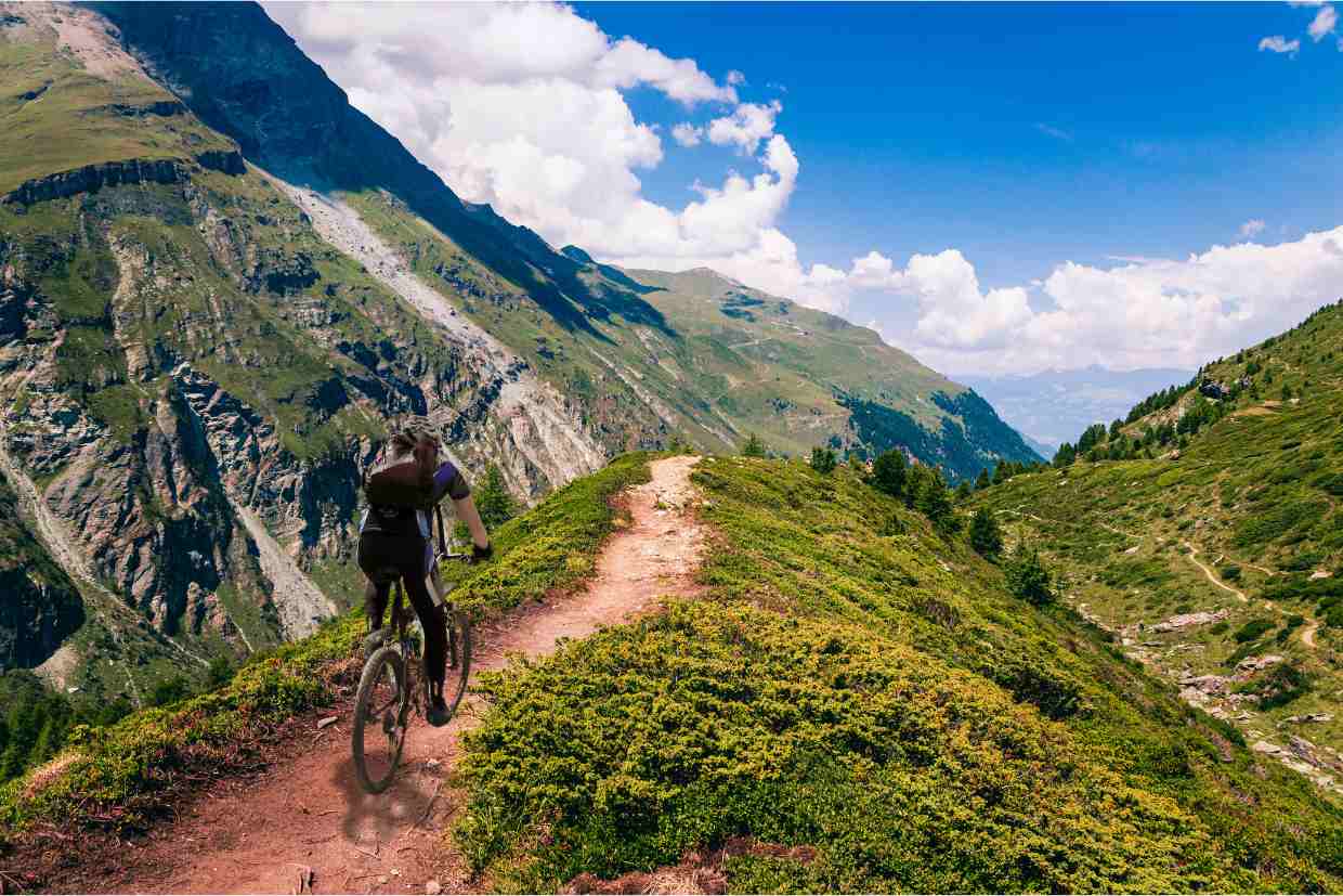 Ciclista em trilha estreita no alto de montanha, mostrando resistência ao pedalar em subidas com mountain bike.