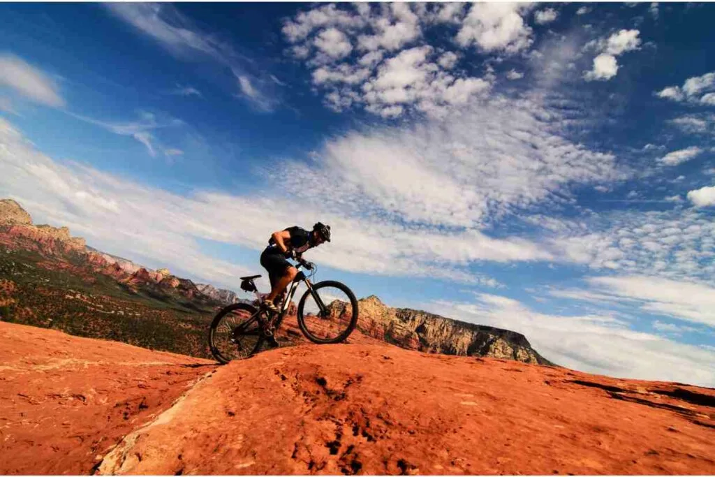Ciclista pedalando em subida íngreme sobre pedras vermelhas no deserto, ilustrando a técnica de pedalar em subidas.