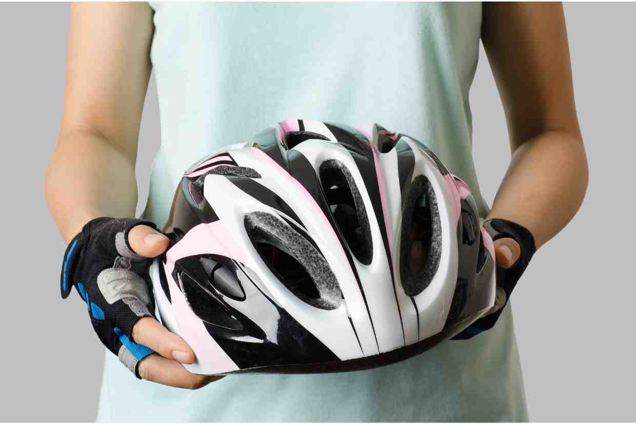 Pessoa segurando um capacete branco com detalhes rosa e preto nas mãos, simbolizando cuidado e atenção à validade do capacete de ciclismo.