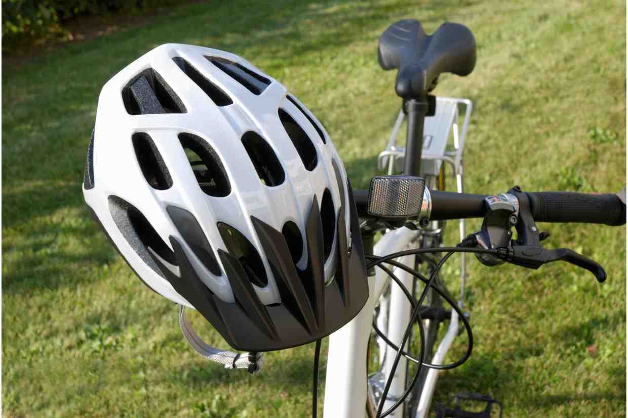 Capacete branco apoiado no guidão de uma bicicleta em um jardim, simbolizando a importância de verificar a validade do capacete de ciclismo antes de cada uso.