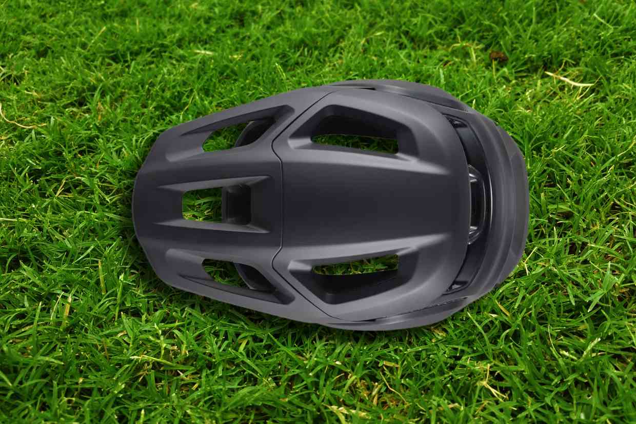 Capacete Specialized Ambush 2 cinza colocado sobre o gramado com seu topo virado para cima, mostrando os detalhes das suas entradas de ar.