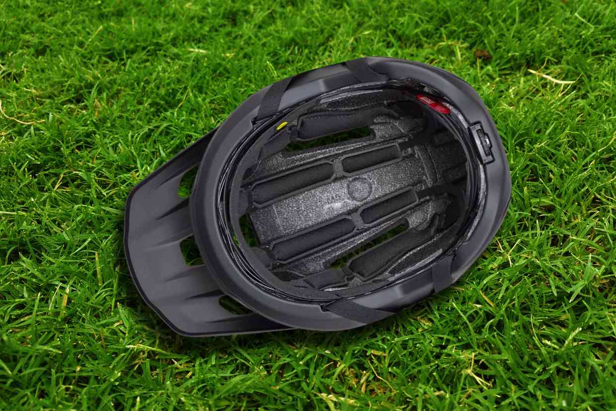 Capacete Specialized Ambush 2 cinza colocado sobre o gramado com seu fundo acolchoado e sistema MIPS mostrados e virados para cima.