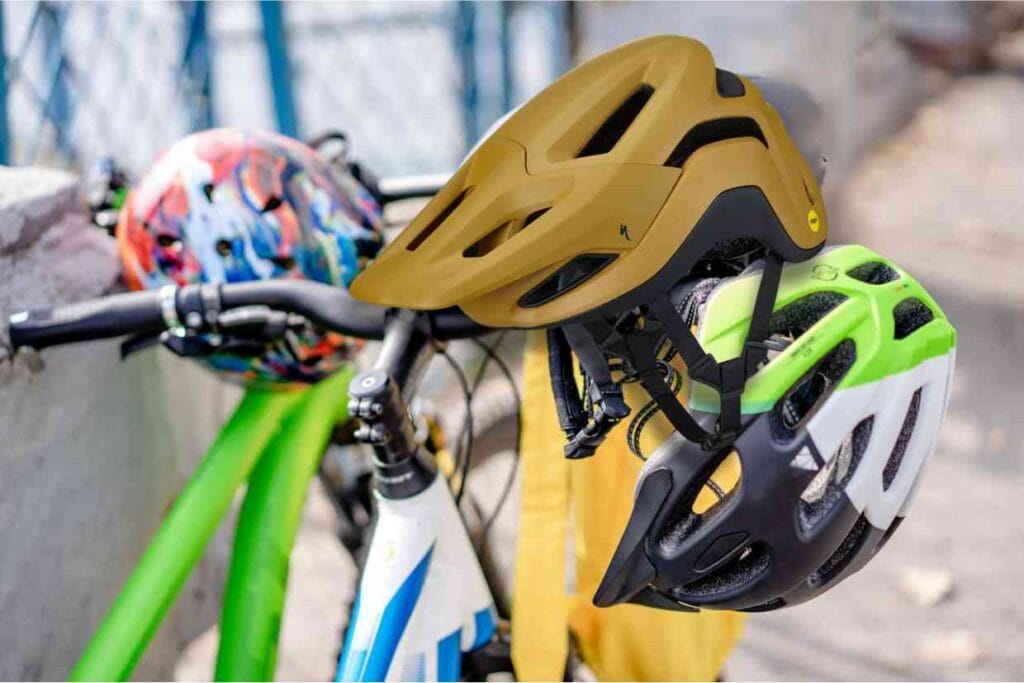 Imagem de bicicleta estacionada junto a uma mureta com três capacetes pendurados no guidão, entre eles, o Specialized Ambush 2.