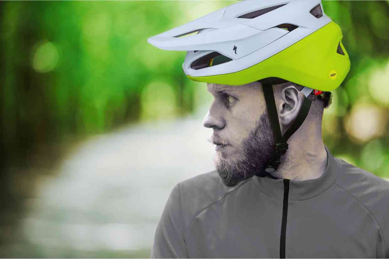 Ciclista olhando na direção da trilha usando uma camisa cinza e uma capacete Specialized Camber verde e branco na cabeça.