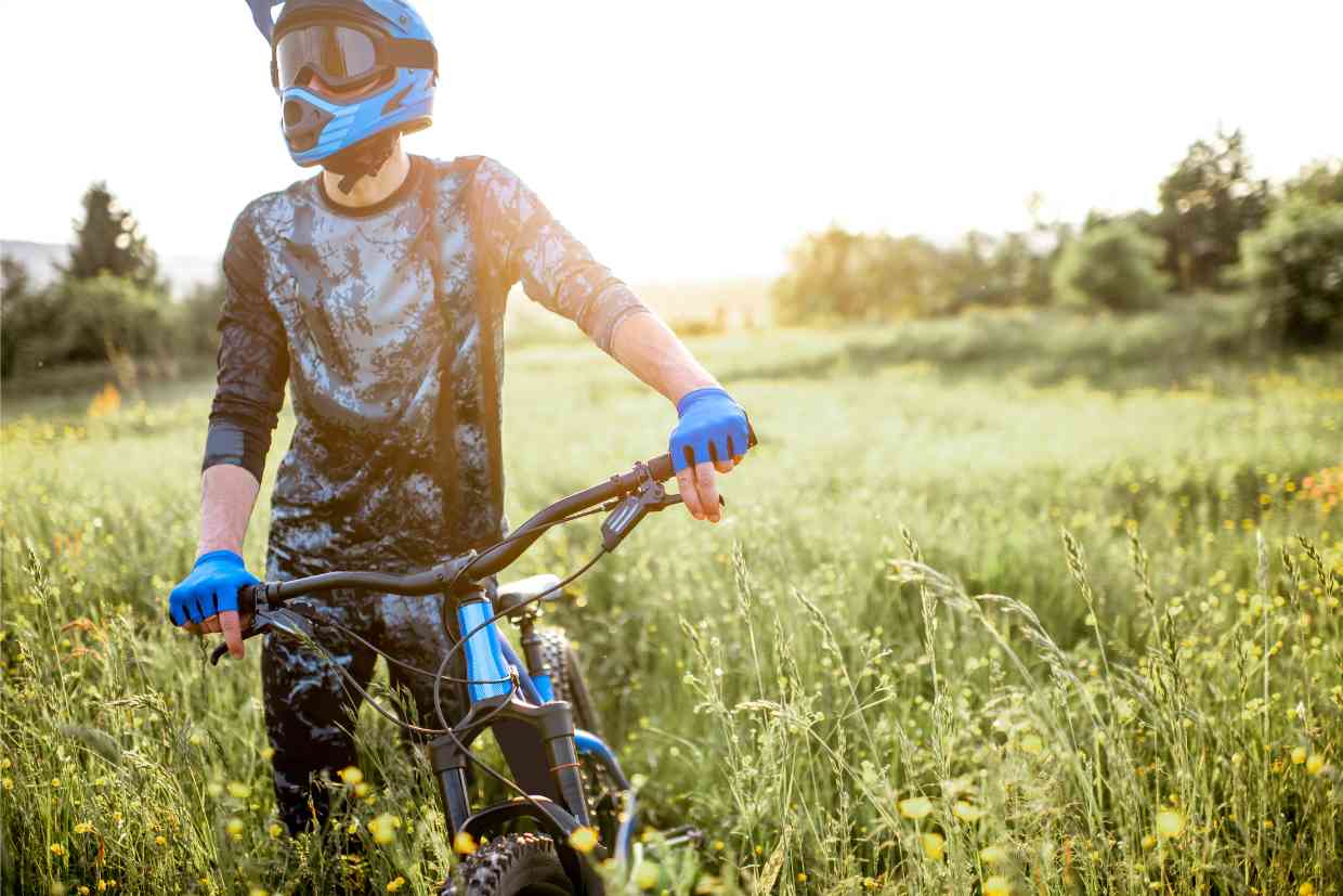 Ciclista descansa segurando sua bike numa trilha fechada com mato alto usando roupas de ciclismo MTB e o capacete GIRO SWITCHBLADE MIPS .
