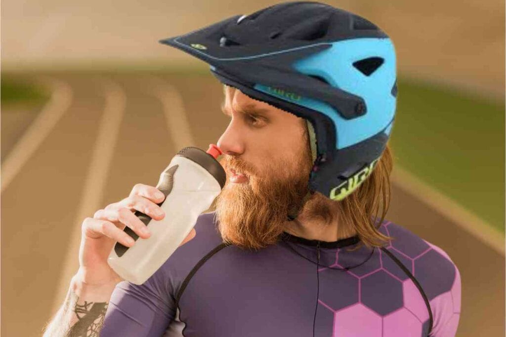 Ciclista se hidratando, usando roupas para ciclismo e vestindo o capacete GIRO SWITCHBLADE MIPS para sua proteção.