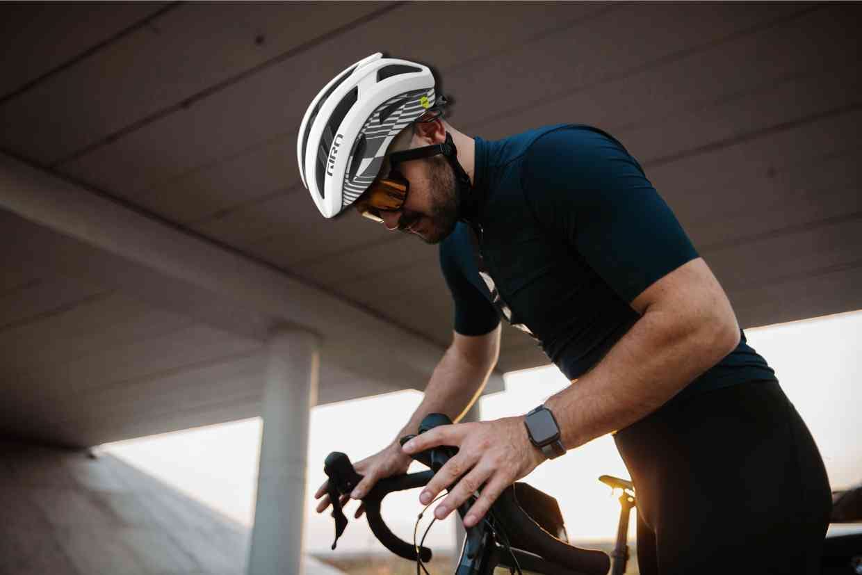 Ciclista de pé, usando seu capacete Giro Aries Spherical enquanto ajusta sua bike.