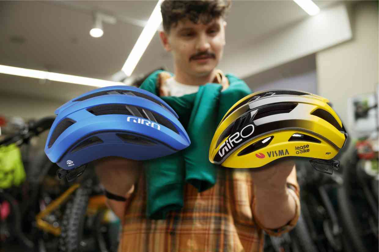 Vendedor de uma bicicletaria exibe dois capacetes Giro Aries Spherical um azul e outro amarelo a um cliente interessado.