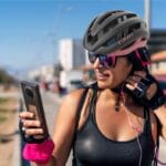 Ciclista usando seu Giro Aries Spherical e óculos de sol olha para a tela do celular enquanto ajusta os fones de ouvido.